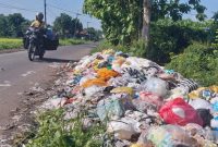 Seorang pengendara sepeda motor melintasi tumpukan sampah di Desa Rempanga